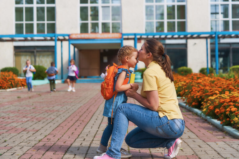 mom kissing her daughter on her first day of school