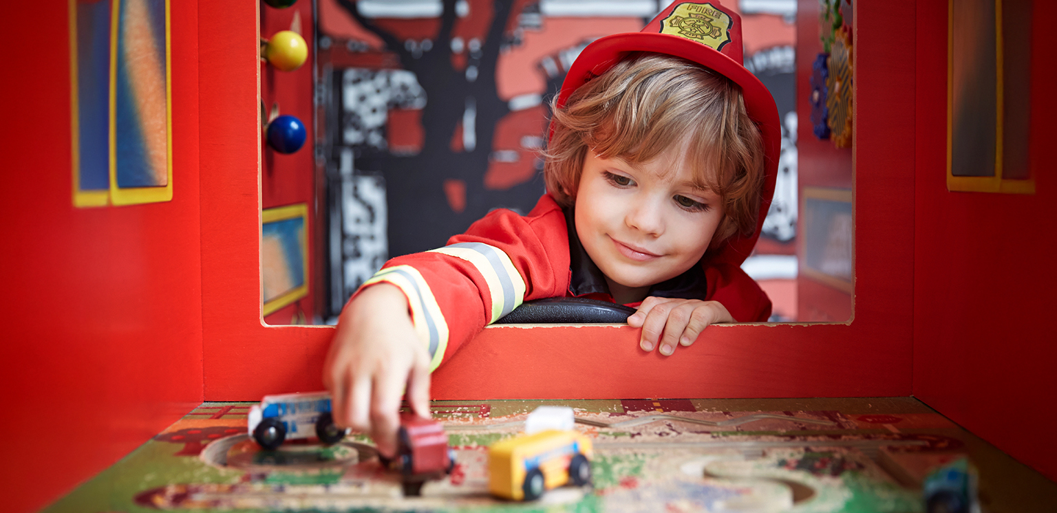 little kid dressed as a firefighter playing with toy firetrucks